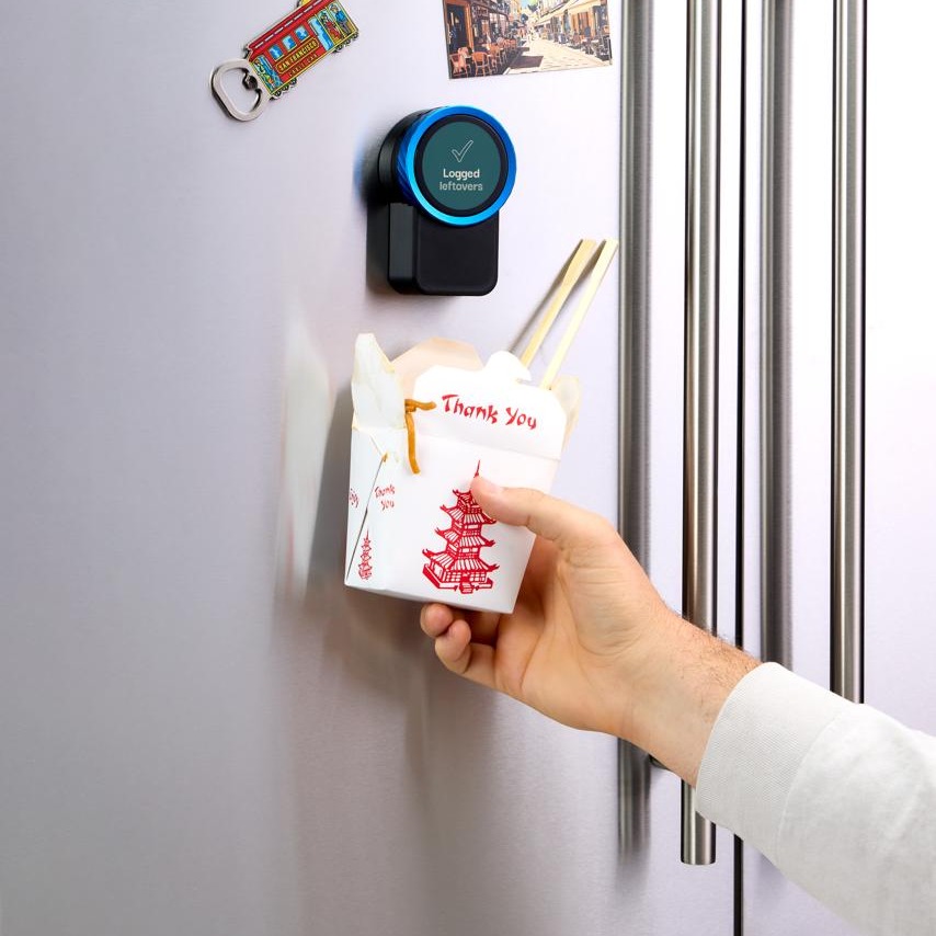 A takeout box held up to the Trepo device on the fridge door, which reads Logged - leftovers